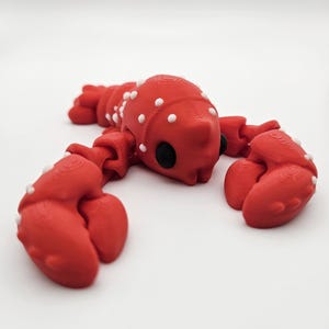 May include: A red lobster figurine with white spots, articulated legs, and black eyes. The lobster is posed with its claws outstretched.