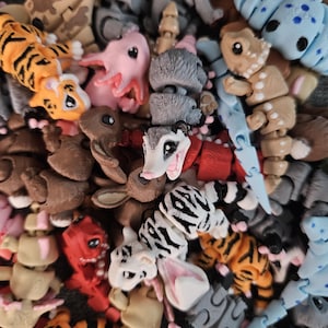 Puede incluir: Una colecci&oacute;n de juguetes de animales articulados y coloridos. El surtido incluye tigres con rayas naranjas y negras, ajolotes rosas, conejos y otras criaturas en varios colores y patrones. Los juguetes parecen ser de pl&aacute;stico.