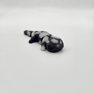 May include: A small, black and white spotted salamander figurine. The figurine is made of a smooth, plastic-like material and has a realistic appearance.