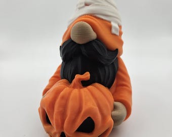 May include: A Halloween gnome figurine with a white bandage on its head, a black beard and mustache, and holding an orange pumpkin with a carved face.