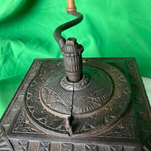 Op de afbeelding: Antiek gietijzeren koffiemolen met een houten kruk. De molen heeft een decoratief ontwerp aan de bovenkant en een lade eronder.