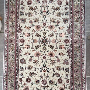 May include: A white rug with a floral pattern in shades of pink, green, and brown. The rug has a fringe border.