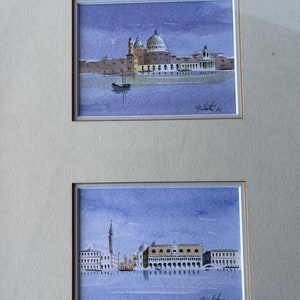 May include: Two watercolor paintings of Venice, Italy. The top painting shows a view of the city with a church in the background. The bottom painting shows a view of the city with a bell tower in the background.