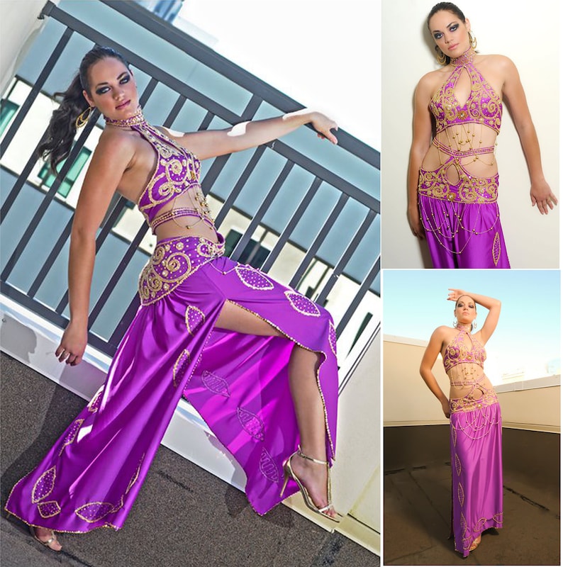 May include: A woman wearing a purple and gold belly dancing costume. The costume features a halter top, a skirt with a slit, and a belt with gold embellishments.
