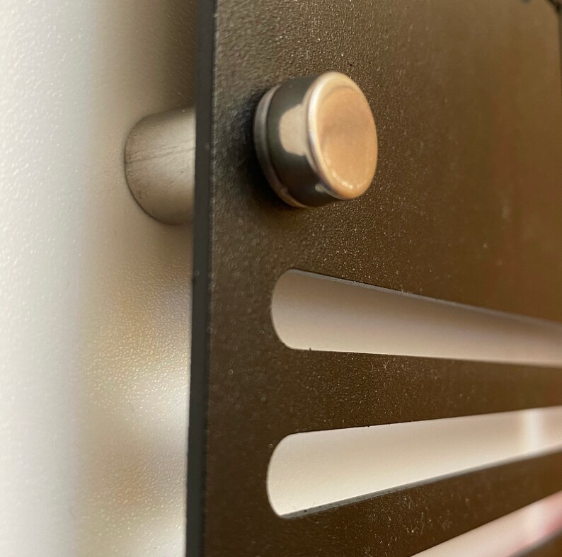 May include: Close-up of a black metal wall mount with two horizontal slots. The mount is attached to a white wall with two silver metal screws.