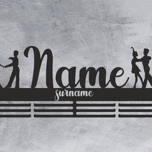 May include: Black metal wall-mounted medal display with a silhouette of two dancers. The display has a personalized name and surname.