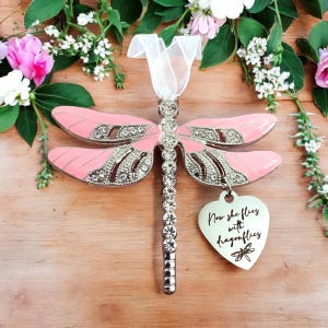 May include: Pink dragonfly ornament with rhinestones and a silver heart charm that reads "Now she flies with dragonflies".