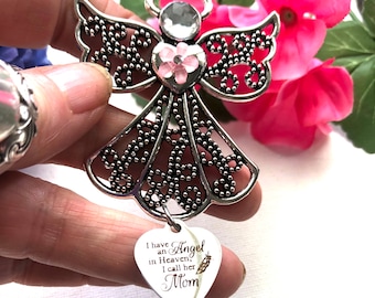 May include: Silver angel ornament with a pink flower heart and a crystal in the center. The angel has a heart-shaped tag that reads "I have an Angel in Heaven, I call her Mom".