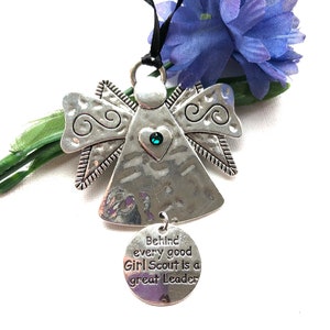 May include: Silver angel ornament with a green gem heart and a round charm that reads "Behind every good Girl Scout is a great Leader".