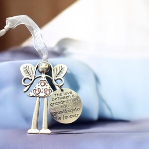 May include: Silver angel figurine with pink rhinestones, holding a round charm that reads "the love between a grandmother and granddaughter is forever".