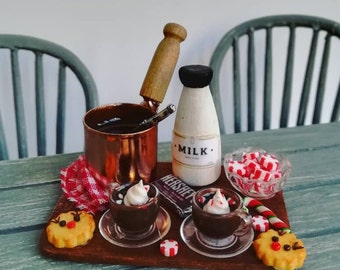 May include: A miniature scene of a holiday hot chocolate bar with two mugs of hot chocolate topped with whipped cream and candy canes, a small pot of hot chocolate, a bottle of milk labeled "MILK", a bowl of red and white candy canes, and two gingerbread cookies.