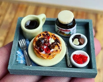 May include: A miniature breakfast tray with a cup of coffee, a plate of pancakes topped with chocolate sauce, whipped cream, and raspberries, a jar of Nutella, a small bowl of chocolate hearts, and a small bowl of red berries.