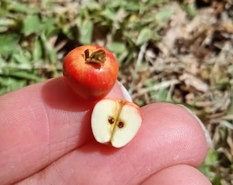 May include: Two miniature red apples, one whole and one cut in half, showing the inside of the apple with seeds.