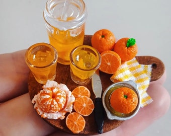 May include: A miniature set of orange juice and oranges on a wooden tray. The set includes a glass pitcher, two glasses, and several oranges, including a peeled orange.