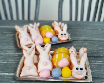 May include: A tray of white bunny-shaped cookies decorated with pastel-colored icing and candy. The cookies are arranged on a tray with a white background.