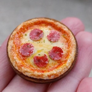 Könnte beinhalten: Miniaturpizza mit fünf Peperoni-Scheiben auf einem Holzsockel. Die Pizza hat einen goldenen Kruste, geschmolzenen Käse und eine rote Soßenbasis. Ein kleines, detailliertes Lebensmittel.