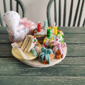 Op de afbeelding: Een miniatuur verjaardagstaart met kleurrijke sprinkels, kaarsen en een stuk taart op een bord. Er zijn ook twee kleine cadeautjes verpakt in blauw en roze lint.