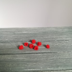 May include: Eight red raspberries on a grey wooden surface.