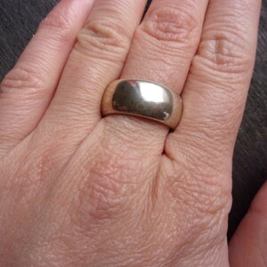 May include: A silver band ring with a smooth, polished finish. The ring is wide and has a rounded shape.