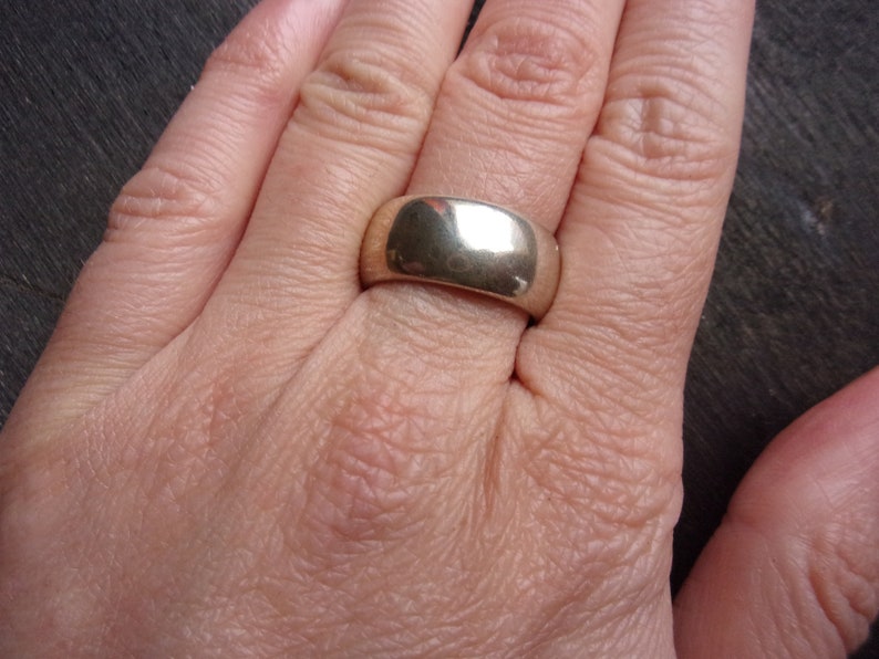 May include: A silver band ring with a smooth, polished finish. The ring is wide and has a rounded shape.