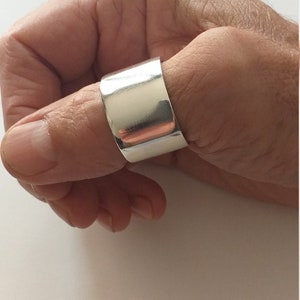 Peut inclure: Une bague de pouce en argent avec une bande large et plate.