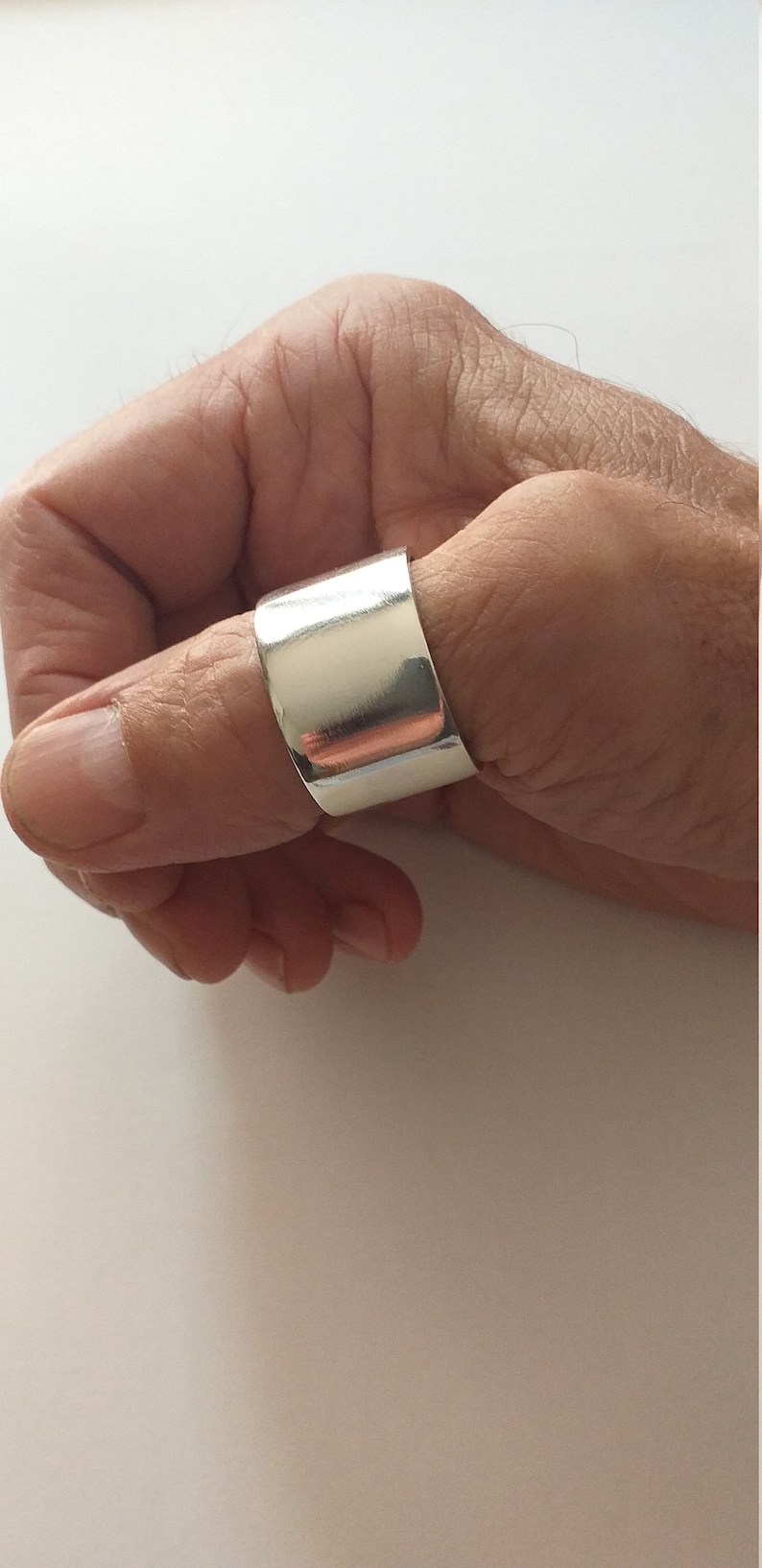 Peut inclure: Une bague de pouce en argent avec une bande large et plate.