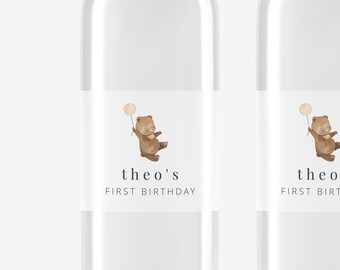 May include: Three clear plastic water bottles with labels that say "theo's first birthday" and feature a cartoon illustration of a brown bear holding a balloon.