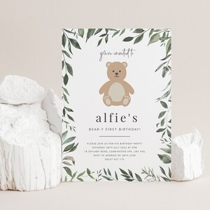 Puede incluir: Una tarjeta de invitaci&oacute;n blanca con un borde de hojas verdes y una ilustraci&oacute;n de un oso de peluche marr&oacute;n. El texto en la tarjeta dice "you're invited to alfie's BEAR-Y FIRST BIRTHDAY! PLEASE JOIN US FOR HIS BIRTHDAY PARTY SATURDAY 28TH JULY 2022 AT 3PM 18 SKYLARK ROAD, LEAMINGTON SPA, LM2 480 RSVP TO GEORGE BATH JUNE 09247 927 175"
