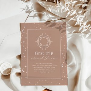 May include: A light brown invitation card with a white sun and moon design. The text on the card reads "first trip around the sun" and "Archer is turning one".
