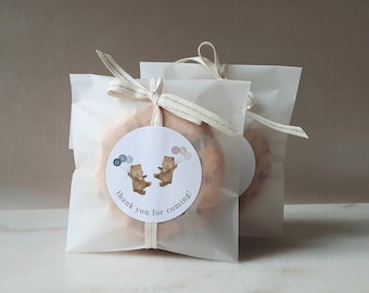 May include: Two small brown teddy bears holding balloons with the word "one" on them. The bears are on a white circle sticker with the text "thank you for coming!" on a clear cellophane bag with a white ribbon.