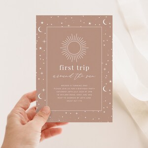 May include: A light brown invitation card with a white sun and moon design. The text reads "first trip around the sun" and includes details for a birthday party.