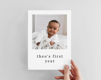Op de afbeelding: Een witte kaart met een foto van een baby in een wit rompertje. De tekst "theo's first year" staat onder de foto.