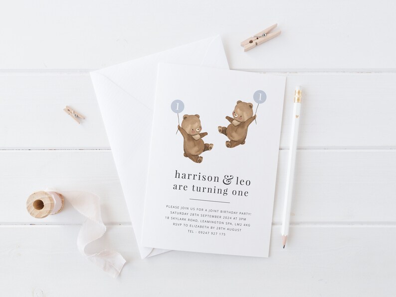 May include: A white invitation card featuring a brown bear illustration holding a blue balloon with the number one on it. The text on the card reads "harrison & leo are turning one". The invitation includes details for a joint birthday party.