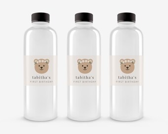 May include: Three clear plastic water bottles with labels featuring a brown bear wearing a white flower crown. The labels also say "tabitha's first birthday".