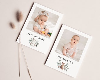 May include: Two white cards with photos of a baby at five and six months old. The cards have a floral design with a bunny and a deer on each card. The text "five months" and "six months" is printed on each card.