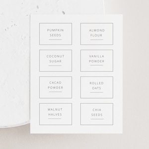 May include: Eight white labels with black text, each with a different ingredient name. The labels read: Pumpkin Seeds, Almond Flour, Coconut Sugar, Vanilla Powder, Cacao Powder, Rolled Oats, Walnut Halves, Chia Seeds.