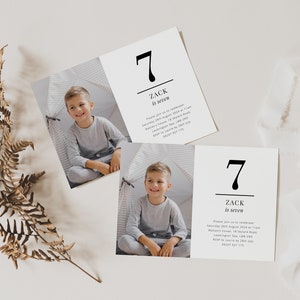 Op de afbeelding: Twee witte kaarten met zwarte tekst en een foto van een jonge jongen. De tekst op de kaarten luidt "7 Zack is zeven". De kaarten liggen op een wit oppervlak met een bruine varen en een spoel wit lint.