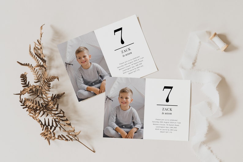 Op de afbeelding: Twee witte kaarten met zwarte tekst en een foto van een jonge jongen. De tekst op de kaarten luidt "7 Zack is zeven". De kaarten liggen op een wit oppervlak met een bruine varen en een spoel wit lint.