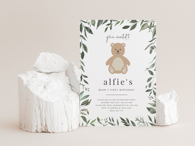 Puede incluir: Una tarjeta de invitaci&oacute;n blanca con un borde de hojas verdes y una ilustraci&oacute;n de un oso de peluche marr&oacute;n. El texto en la tarjeta dice "you're invited to alfie's BEAR-Y FIRST BIRTHDAY! PLEASE JOIN US FOR HIS BIRTHDAY PARTY SATURDAY 28TH JULY 2022 AT 3PM 18 SKYLARK ROAD, LEAMINGTON SPA, LM2 480 RSVP TO GEORGE BATH JUNE 09247 927 175"