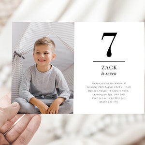 Op de afbeelding: Een witte uitnodigingskaart met zwarte tekst. De kaart toont een foto van een jonge jongen in een grijs shirt en het nummer 7. De tekst luidt "Zack is zeven" en bevat details voor een verjaardagsfeest.