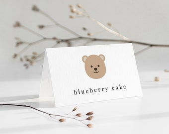 May include: A white card with a brown bear face illustration and the text "blueberry cake" printed in black.