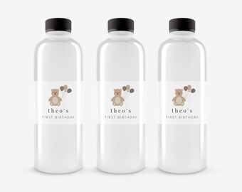 May include: Three clear plastic water bottles with labels that say "theo's first birthday". Each label features a cartoon brown teddy bear holding balloons.