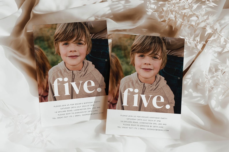 May include: Two white cards with a photo of a young boy on each. The text "five." is printed in large white letters on each card. The cards are on a white and beige fabric background.