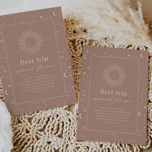 May include: Two brown invitation cards with a white sun and stars design. The text on the cards reads "first trip around the sun".