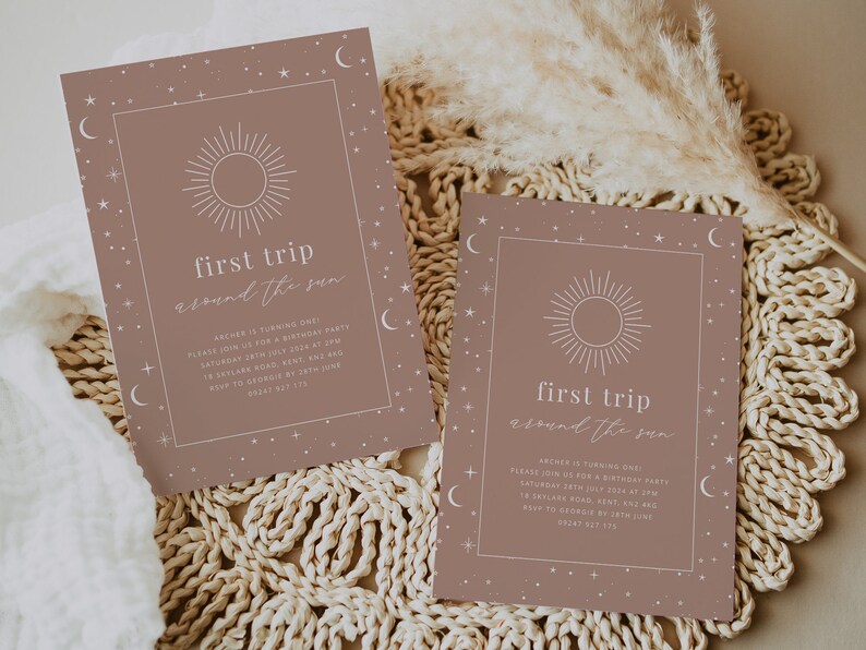 May include: Two brown invitation cards with a white sun and stars design. The text on the cards reads "first trip around the sun".