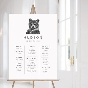 May include: A black and white illustration of a bear cub with the text "HUDSON IS ONE TODAY!"  The illustration is surrounded by a list of milestones, including height, weight, favorite foods, and things the child can do.
