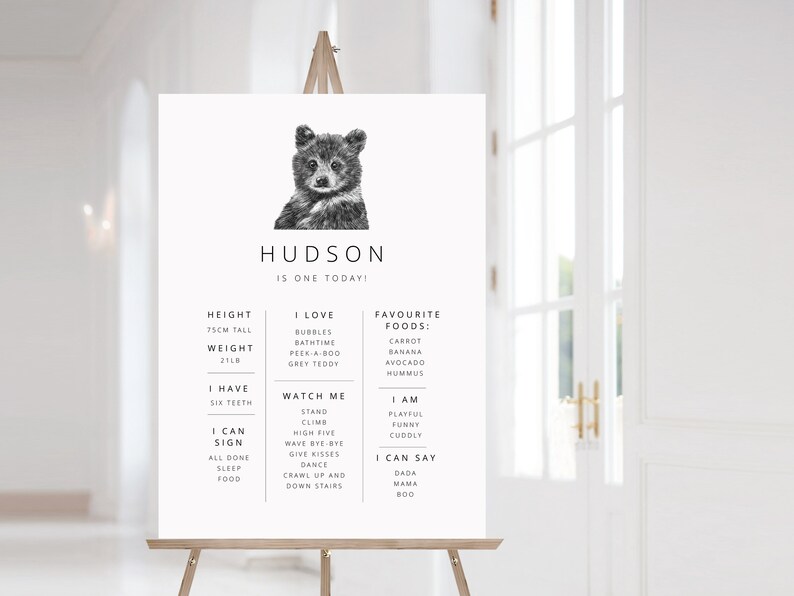May include: A black and white illustration of a bear cub with the text "HUDSON IS ONE TODAY!"  The illustration is surrounded by a list of milestones, including height, weight, favorite foods, and things the child can do.