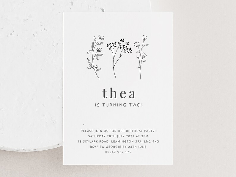May include: A white invitation card with black text and a simple floral illustration. The text reads "thea is turning two!" and includes details for a birthday party.