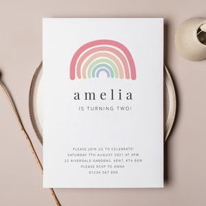 May include: A white invitation card with a rainbow illustration and the text "amelia is turning two!"  The invitation includes details for a birthday party, including the date, time, address, and RSVP information.