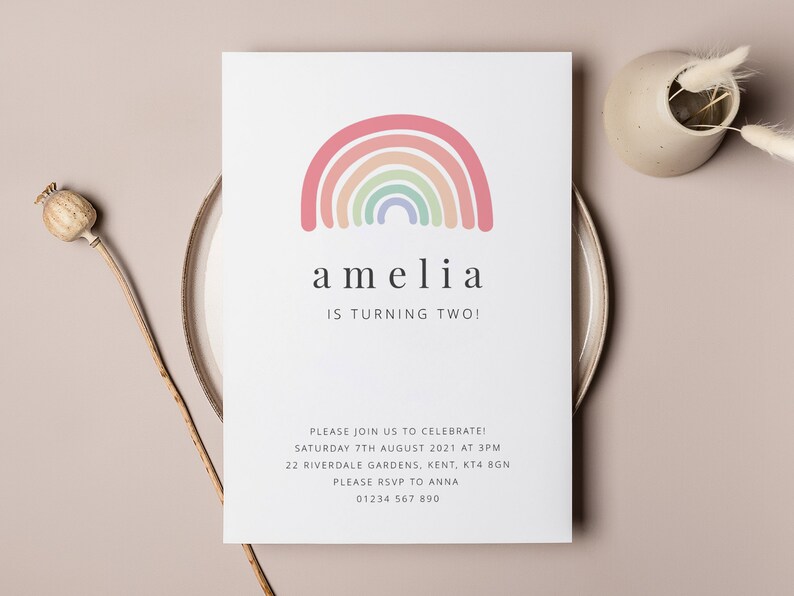 May include: A white invitation card with a rainbow illustration and the text "amelia is turning two!"  The invitation includes details for a birthday party, including the date, time, address, and RSVP information.
